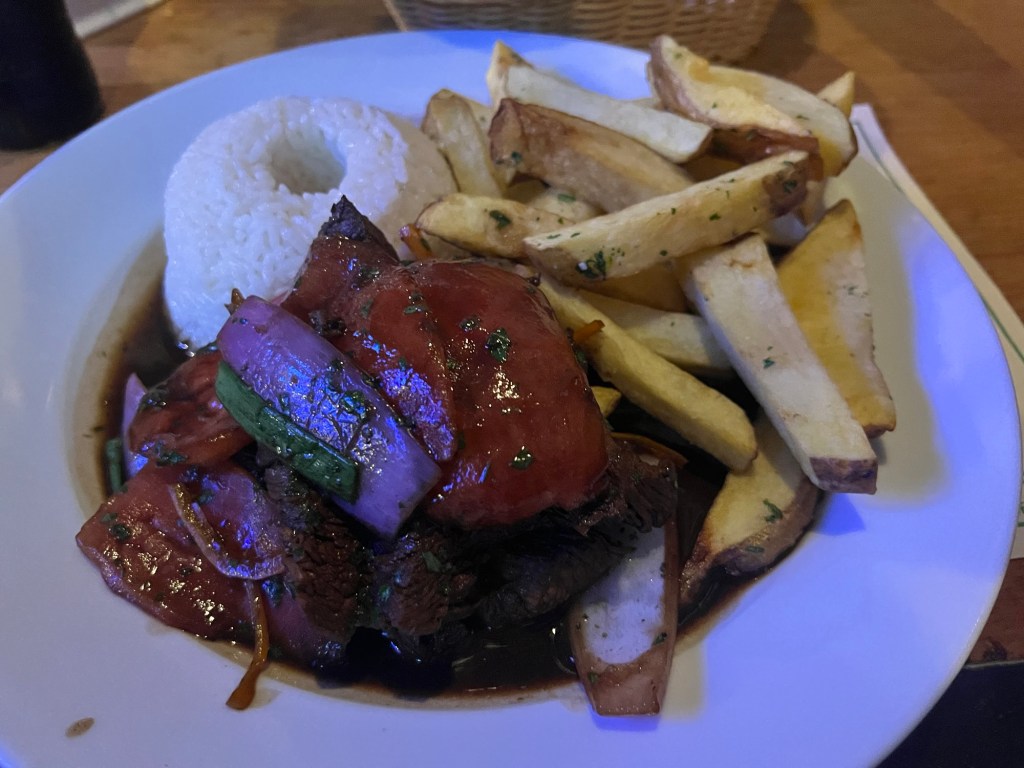 A plate featuring grilled beef topped with sauce and vegetables, accompanied by white rice and French fries.
