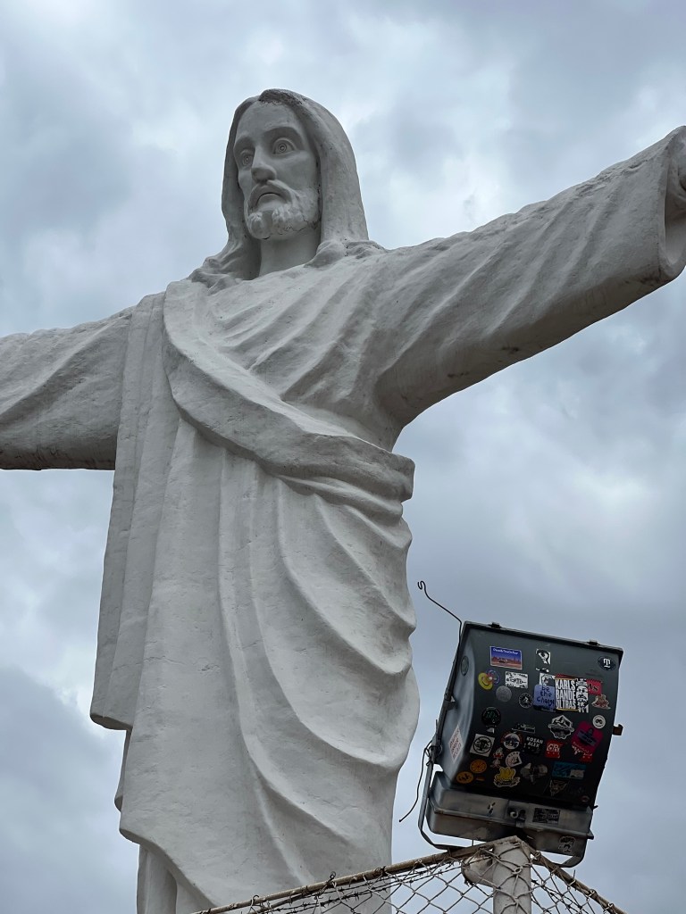 Statue of Cristo Blanco with outstretched arms against a cloudy sky in Cusco, Peru.