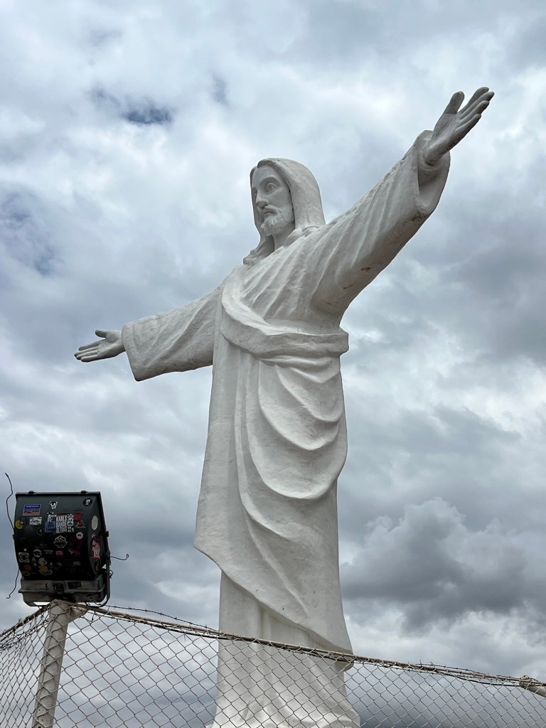 A large white statue of Christ with outstretched arms, against a cloudy sky.