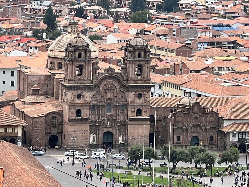 A view of a large historical building with ornate architecture in Cusco, Peru, surrounded by rooftops of the city.